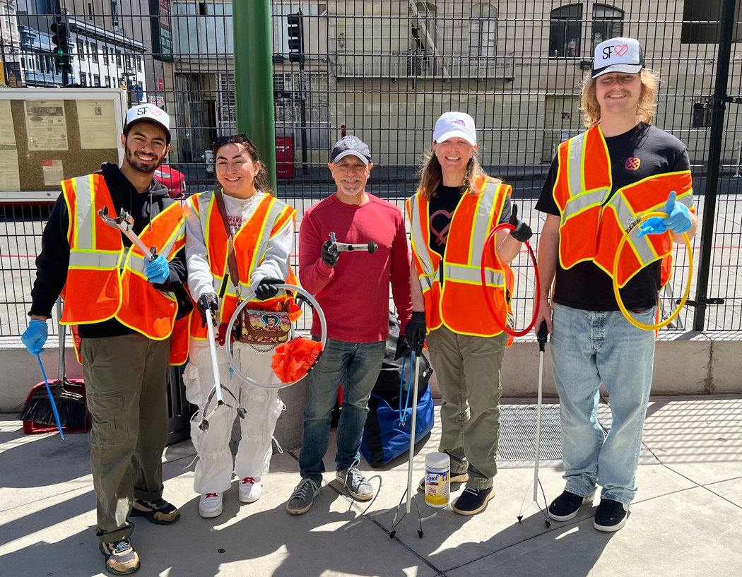 Five SFLuv volunteers in safety vests holding litter grabbers on a Tenderloin sidewalk